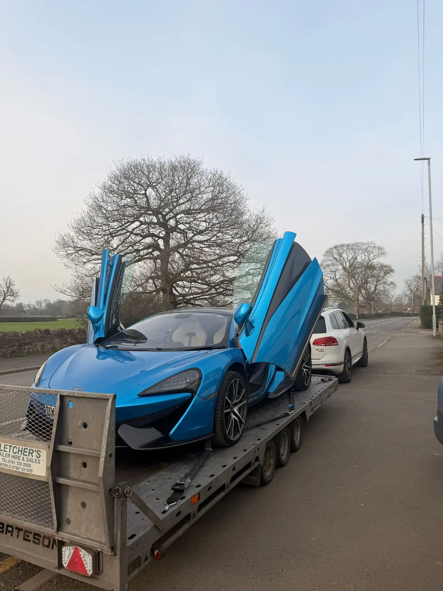 Blue McLaren 570S with dihedral doors open on a Roadway Assist recovery truck